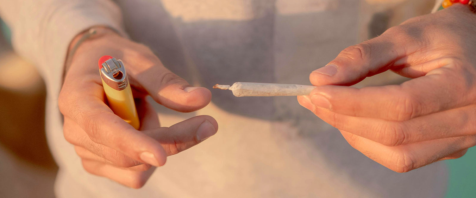 Close-up of a pair of hands holding a weed joint and a lighter in their hands.