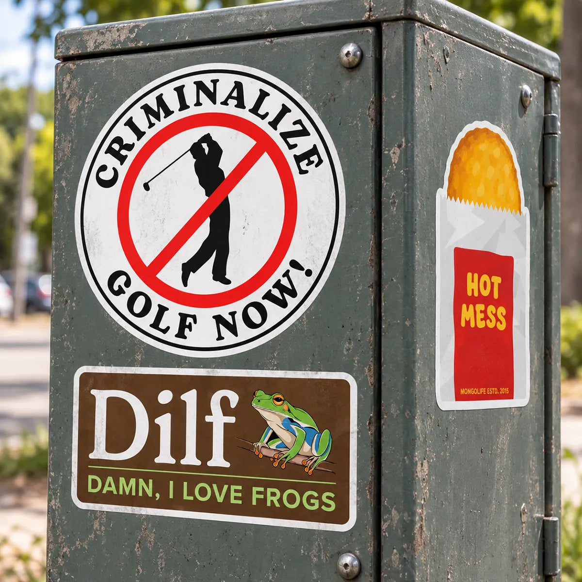 Mongolife graphic stickers featuring Criminalize Golf Now, DILF Damn I Love Frogs, and Hot Mess designs on an outdoor electrical box.