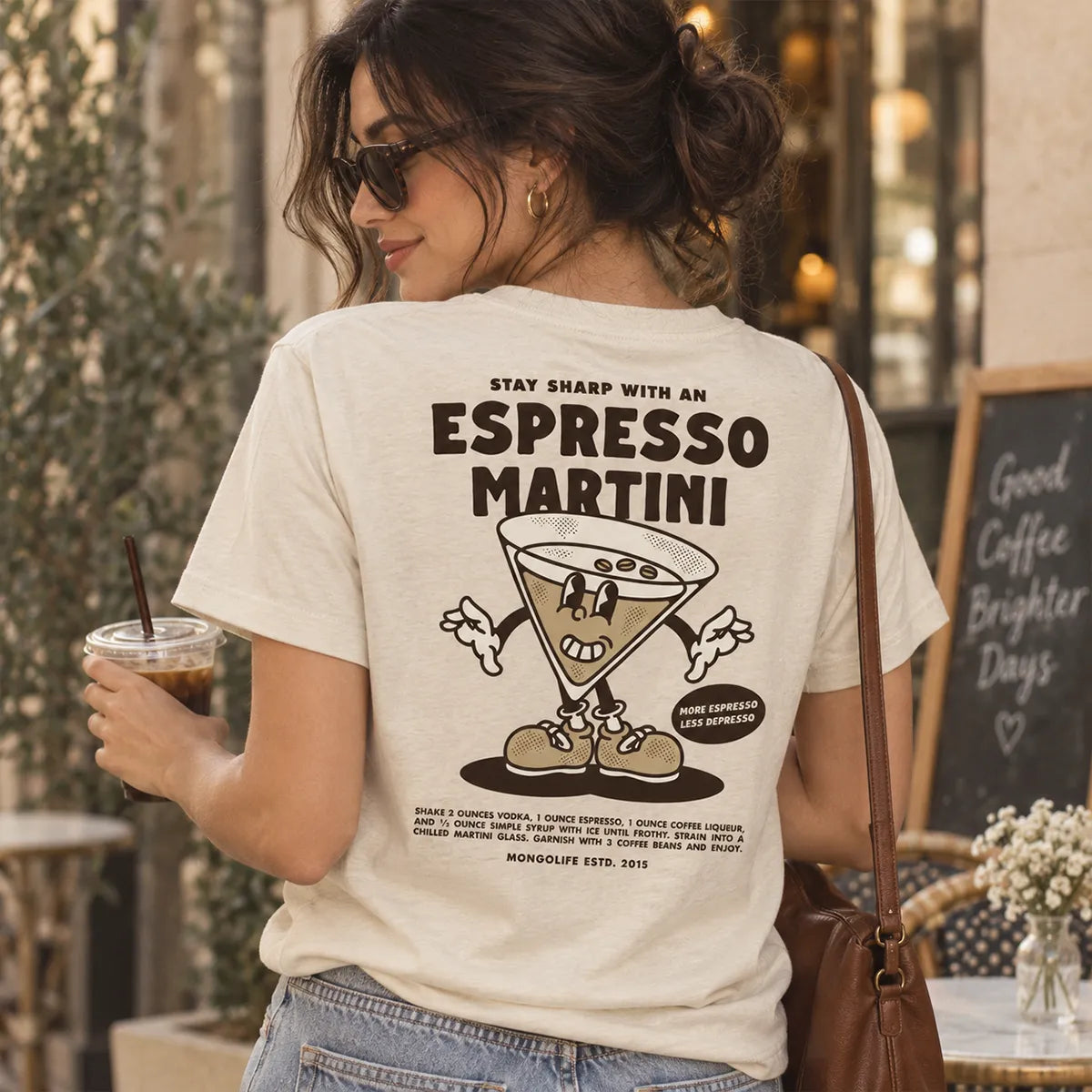 Woman wearing a cream Espresso Martini graphic T-shirt outside a café, shown from the back.