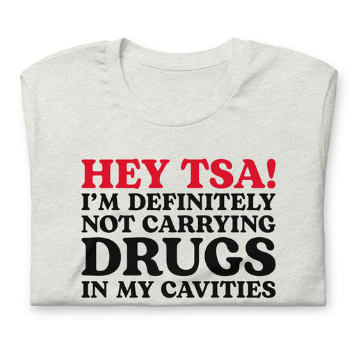 Ash color folded “Hey TSA! I’m Definitely Not Carrying Drugs in My Cavities” prank T-shirt with bold red and black text.