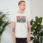 Male model wearing an Ash color “Hey TSA! I’m Definitely Not Carrying Drugs in My Cavities” prank T-shirt with bold red and black text.