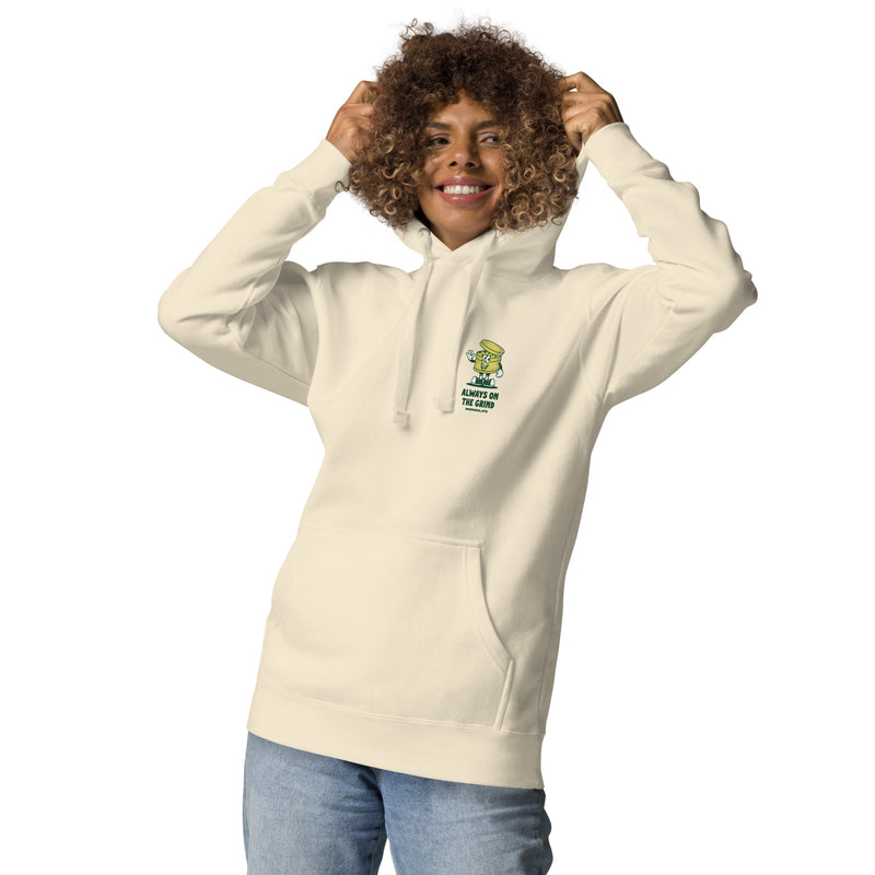 Female model wearing a beige Always on the Grind hoodie, showing the front chest grinder print.