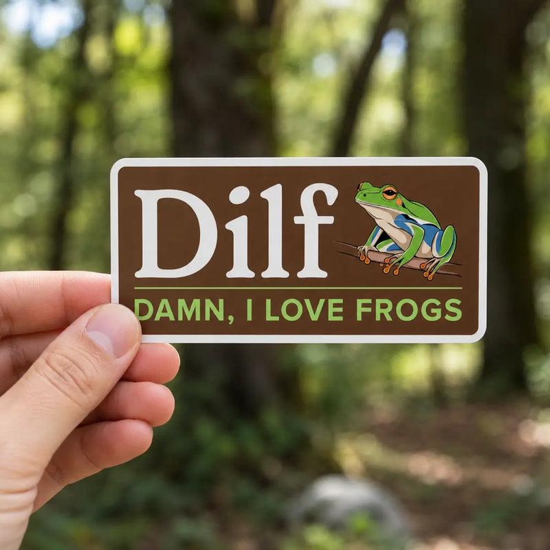 Hand holding a “Dilf, Damn I Love Frogs” sticker with a green frog illustration in front of a softly blurred forest background.