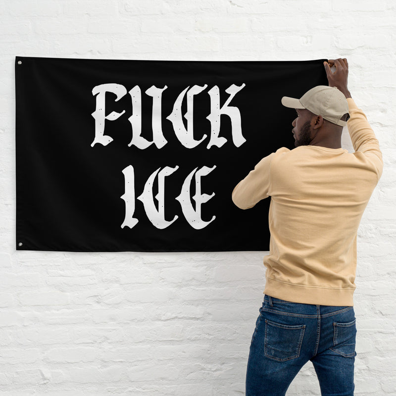 Person pinning a “Fuck ICE” flag to a white wall
