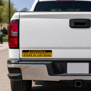 Yellow caution-style prank bumper sticker reading “This vehicle frequently stops at gay bars” on the rear of a white pickup truck.