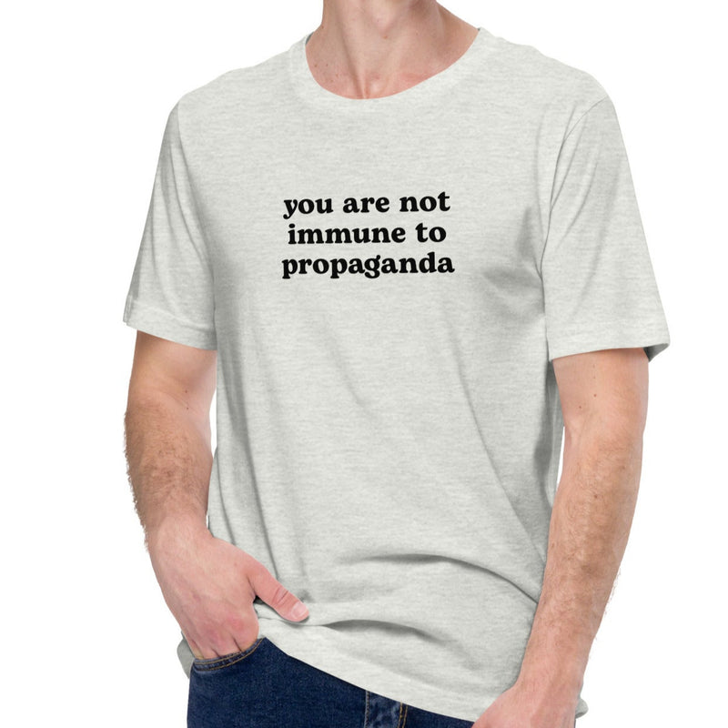A male model wearing the ash grey t-shirt, casually styled with the bold statement print "You are not immune to propaganda"