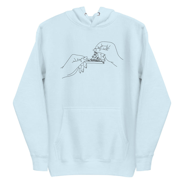 Black and white line art of two hands rolling a joint with flowers, meticulously embroidered on the front chest of a soft, sustainable baby blue hoodie.